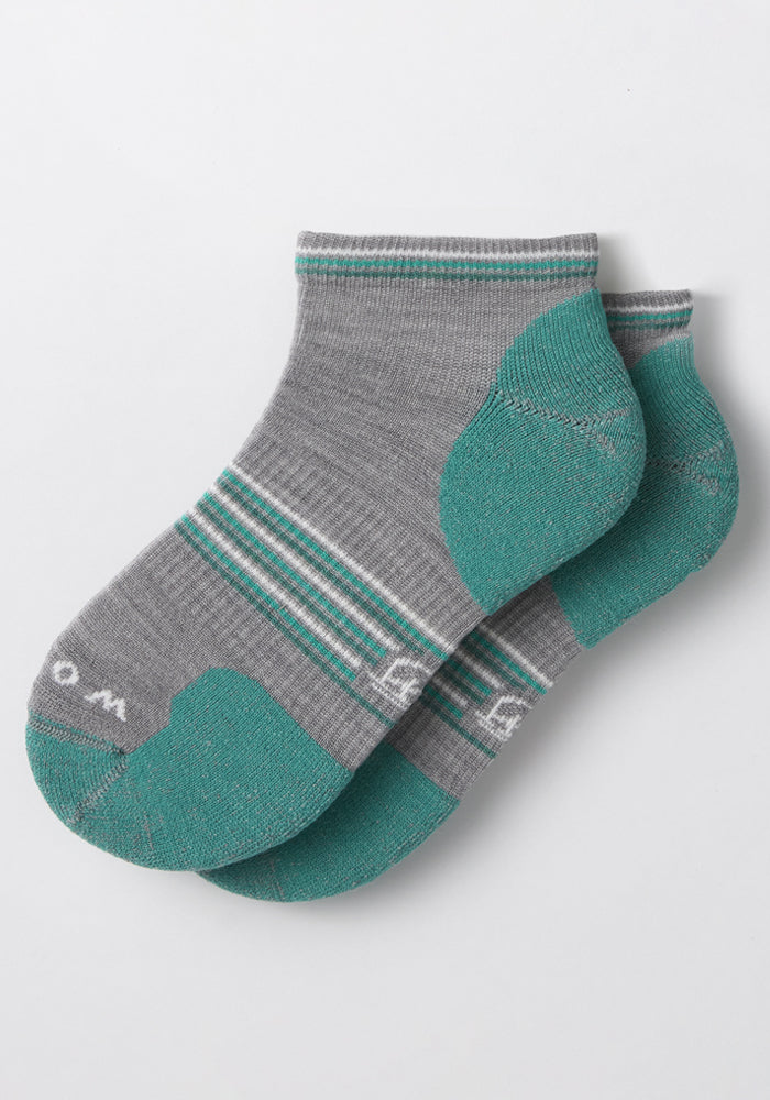 A pair of Woolx Womens Amelia No Show Socks in grey, made from odor-resistant Merino wool, with green toes, heels, and cuffs plus white and green stripes. The socks are neatly stacked on a white background.