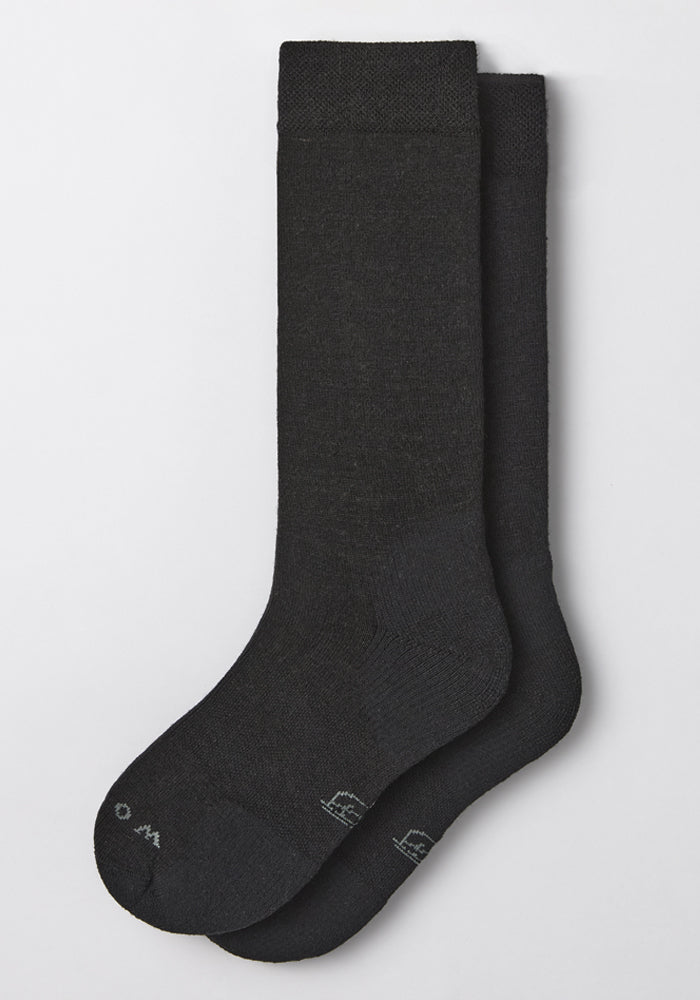 A pair of Woolx Mens Chandler Mid Calf Socks in black are laid flat on a white surface, with one sock slightly overlapping the other. Subtle branding is visible near the toe area.