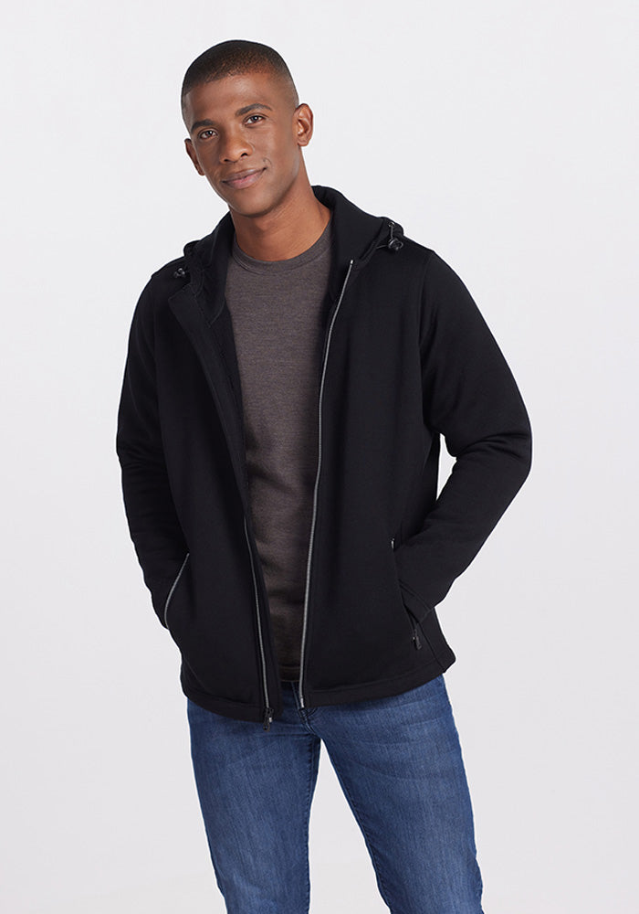 A man wears a black Woolx Grizzly Sweatshirt zip-up hoodie over a dark t-shirt and blue jeans.