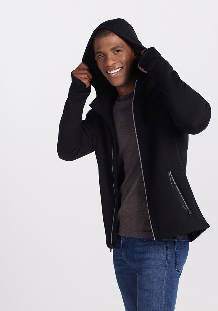 A smiling man wearing a black Woolx Grizzly Sweatshirt, a quick-drying hooded zip-up with zippered pockets.