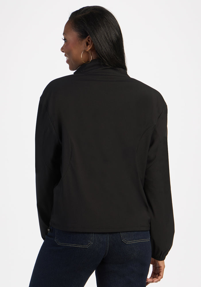 Woman wears the Woolx Cooper Windbreaker in black, featuring zippered pockets, paired with dark jeans, back to camera.