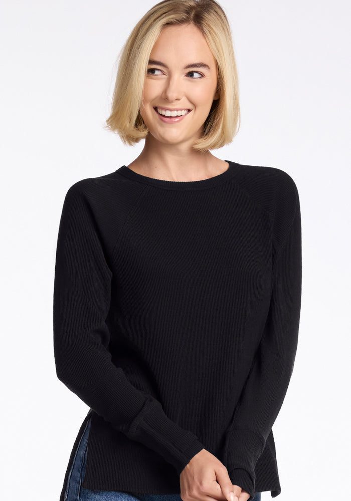Smiling woman with short blonde hair in the Woolx Ainsley Petite Sweater in black, looking sideways on white.
