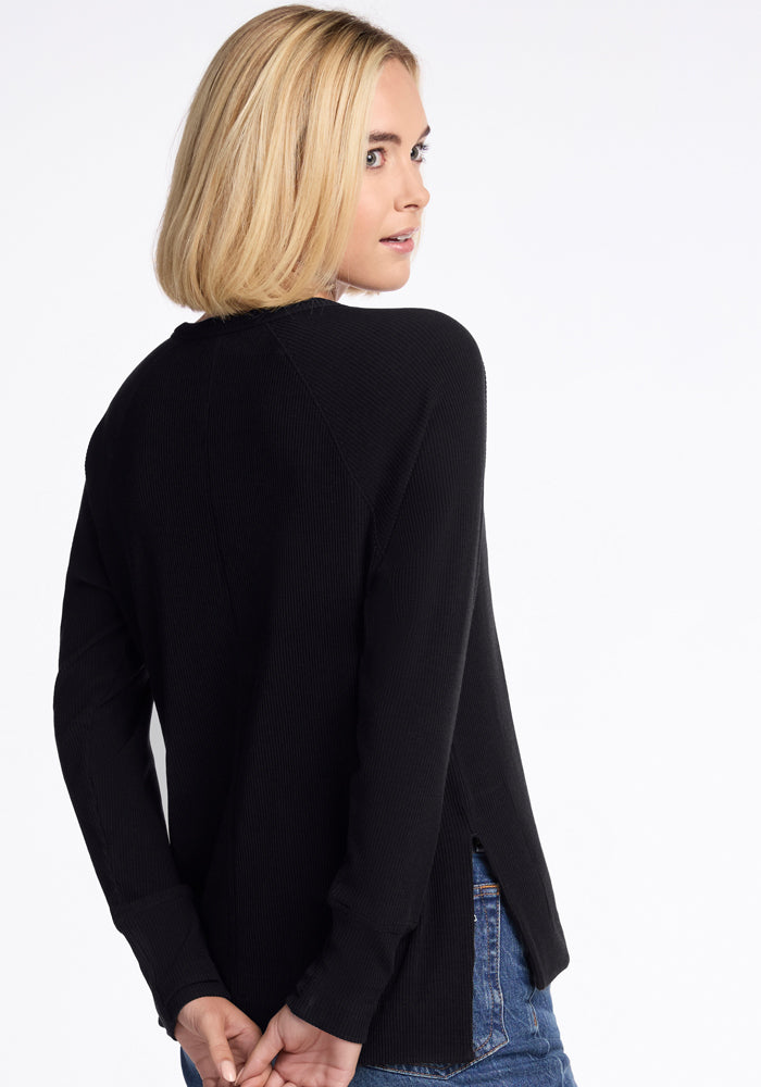 Blonde woman in Woolx Ainsley Petite Sweater - Black, blue jeans, looking over shoulder, hands behind her back.
