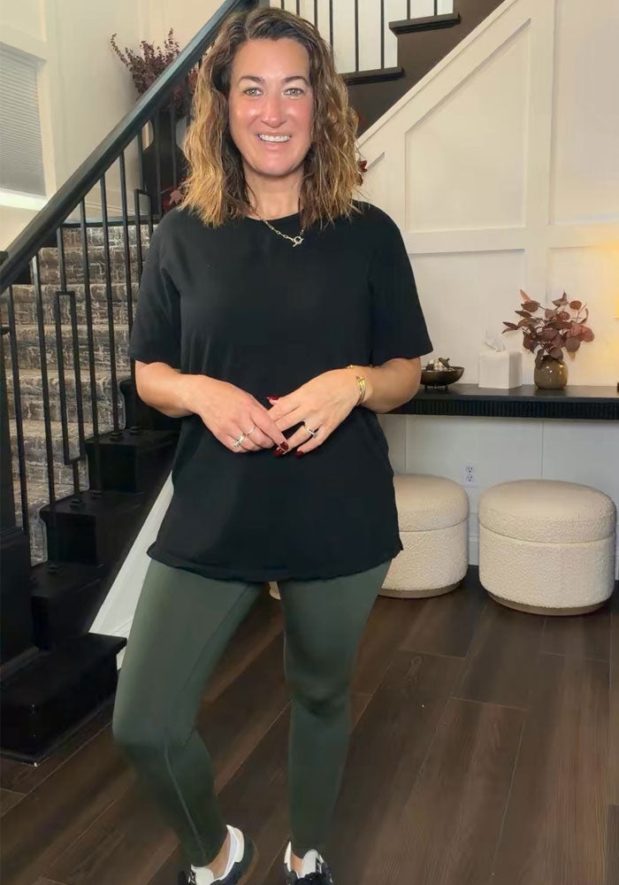 Woman in a black shirt and Woolx Angela Leggings - Everleaf smiles indoors by a staircase and white ottomans.