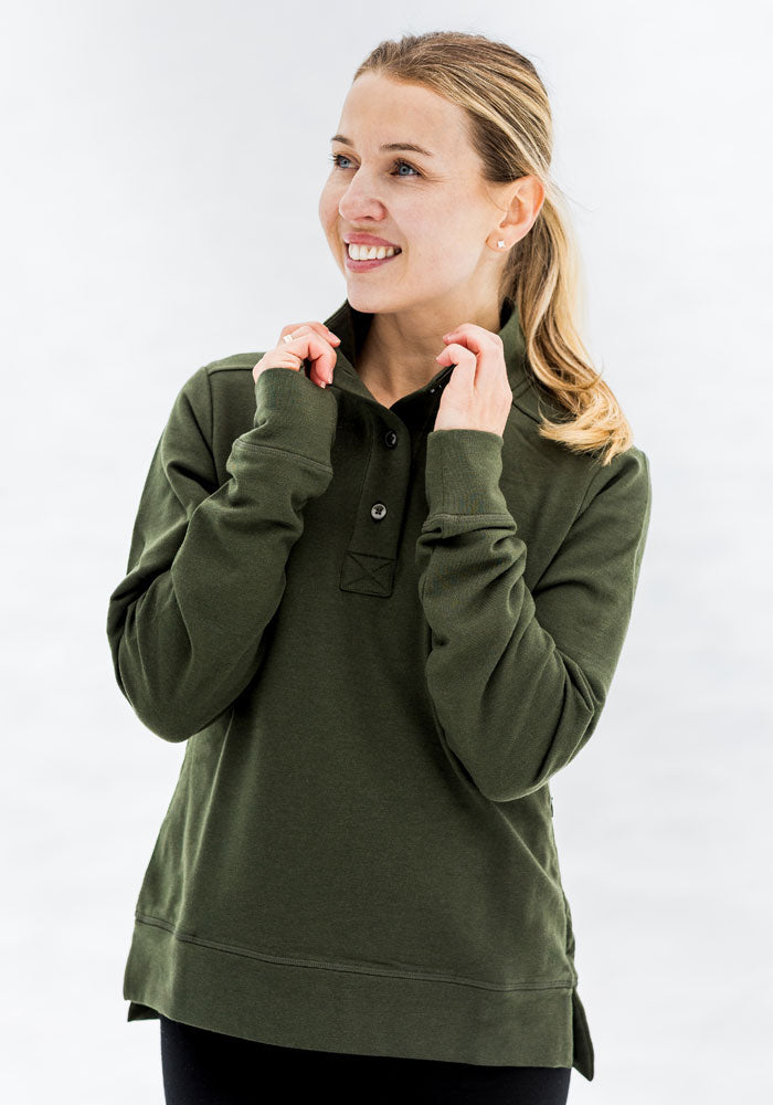 Woman in Woolx Annie 3 Button Pullover - Duffel Bag smiles, hands touching collar, looking away from the camera.
