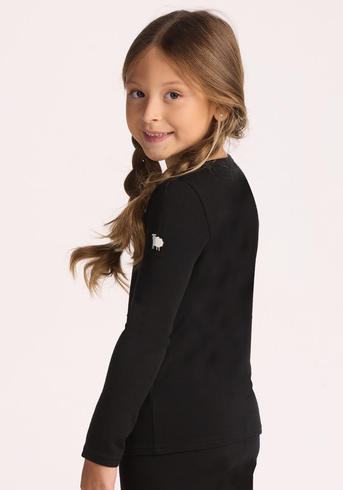 Smiling girl with long, light brown braids wears the Woolx Kids Explorer Base Layer Top in black, made from Australian Merino wool, featuring a white sheep emblem on the sleeve, and looks over her shoulder against a plain background.