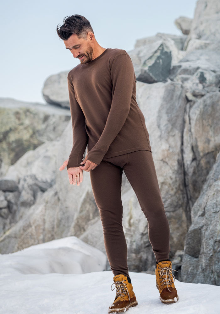 A man in black Woolx Arctic Leggings stands on a rock, dressed for warmth and adventure.