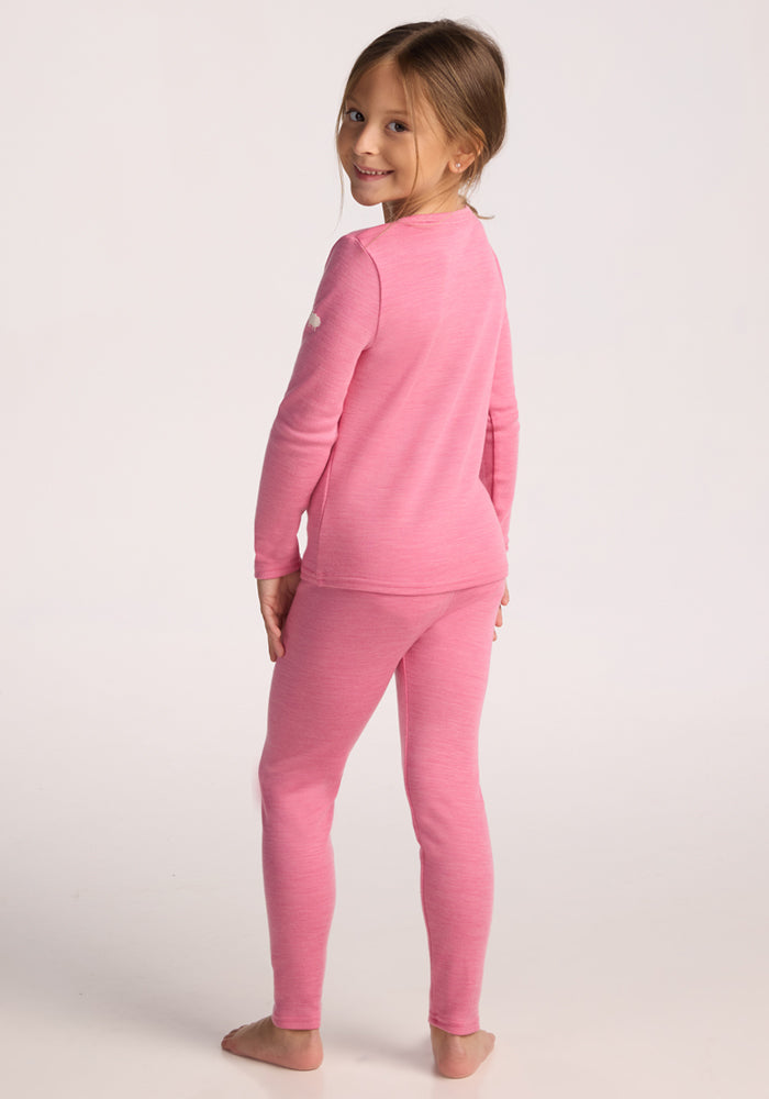 A barefoot girl with long hair smiles over her shoulder, modeling Woolx’s Kids Explorer Base Layer Bottoms - Pinky Promise in pink, paired with a matching long-sleeve top, shown from the back against a plain light background.