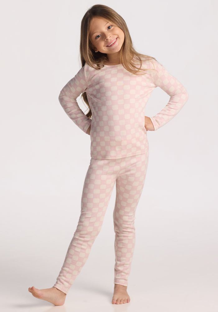 A young girl with long brown hair smiles and poses barefoot, wearing the Woolx Kids Explorer Base Layer Top in Hopscotch Pink against a plain white background.