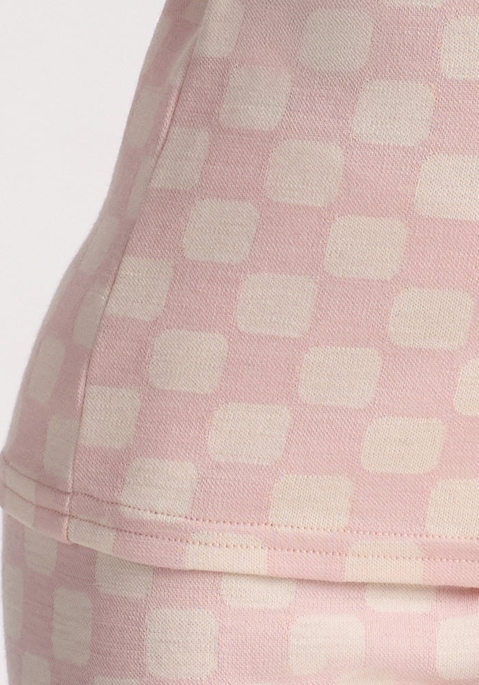Close-up of a child wearing the Woolx Kids Explorer Base Layer Top in Hopscotch Pink, featuring a cream-colored square checkered pattern and crafted from soft, moisture-wicking Australian Merino wool. Only the torso and hip area are visible.