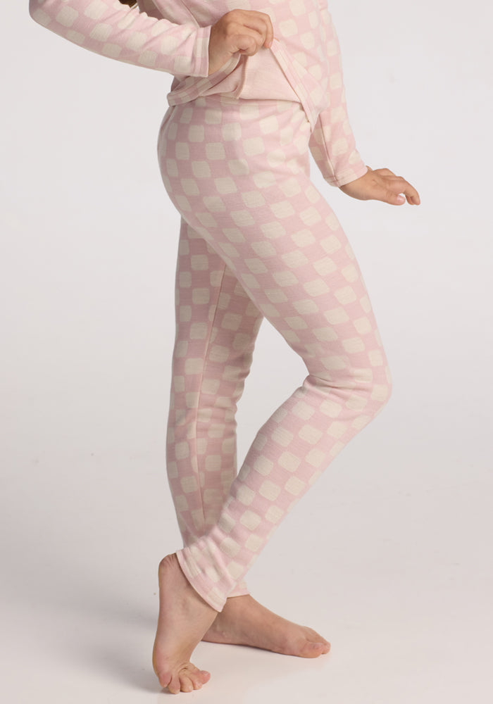 A child models the Woolx Kids Explorer Base Layer Bottoms in Hopscotch Pink, standing barefoot on a white background and showing off the cozy girls' thermal underwear from a side profile.