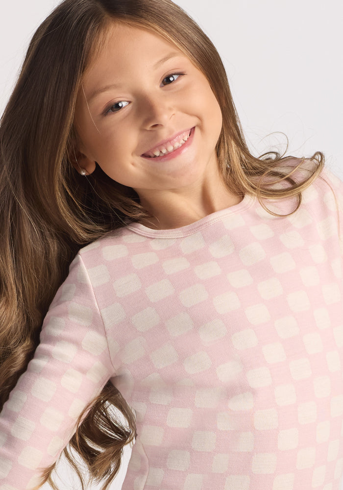 A smiling young girl with long brown hair wears the Woolx Kids Explorer Base Layer Top in Hopscotch Pink, crafted from soft Australian Merino wool, posing against a light background.