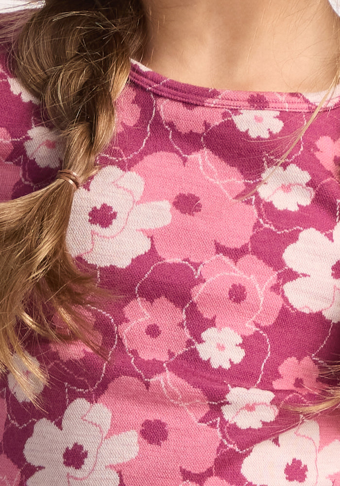 A child’s shoulder and neck, featuring a braid and the Woolx Kids Explorer Base Layer Top - Rosie Posie, a pink Australian Merino wool shirt with a floral pattern in pink and white.