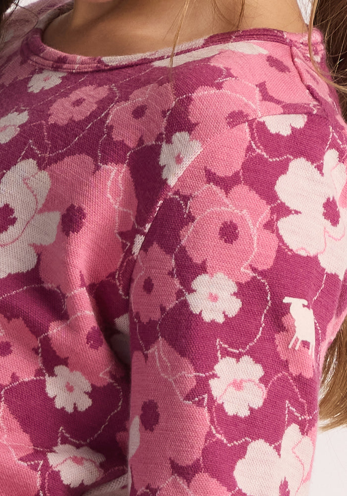 Close-up of the Woolx Kids Explorer Base Layer Top - Rosie Posie, featuring a pink and purple floral pattern with white dog embroidery on the sleeve. Part of a child's brown hair is visible.