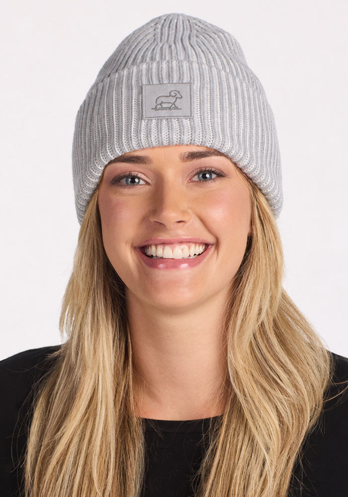 Smiling woman in Woolx Ria Chunky Beanie - Light Ash and black top, shown against a white background.