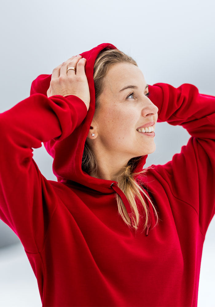 Woman in a Maraschino Cherry Avery Hoodie by Woolx smiles, holding her cozy hood against a light background.