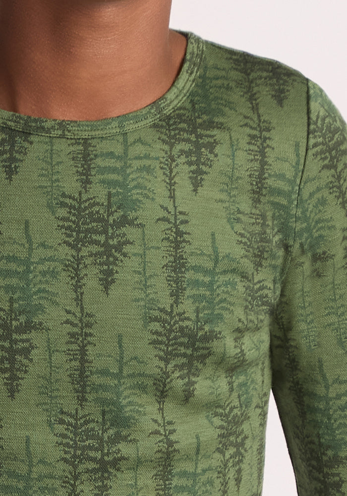 A close-up of a child wearing the Woolx Kids Explorer Base Layer Top - Forest Friends, featuring a green, moisture-wicking fabric with dark green fern leaf patterns; only the lower face, neck, shoulder, and upper chest are shown.