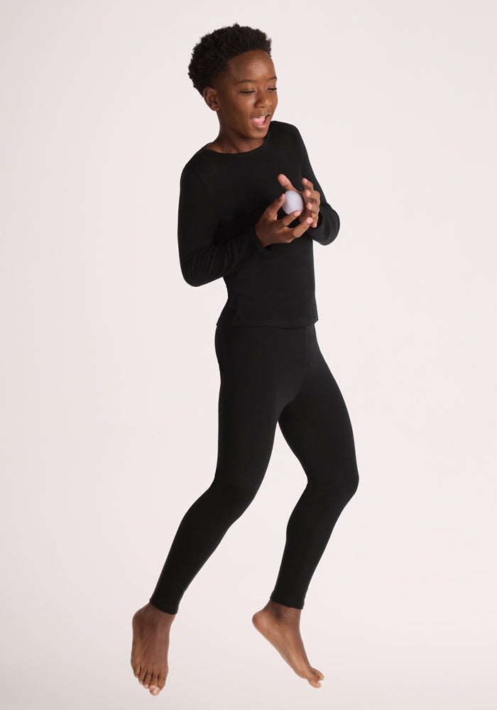 A child wearing Woolx Kids Explorer Base Layer Bottoms in black holds a white object, dressed warmly for the cold.