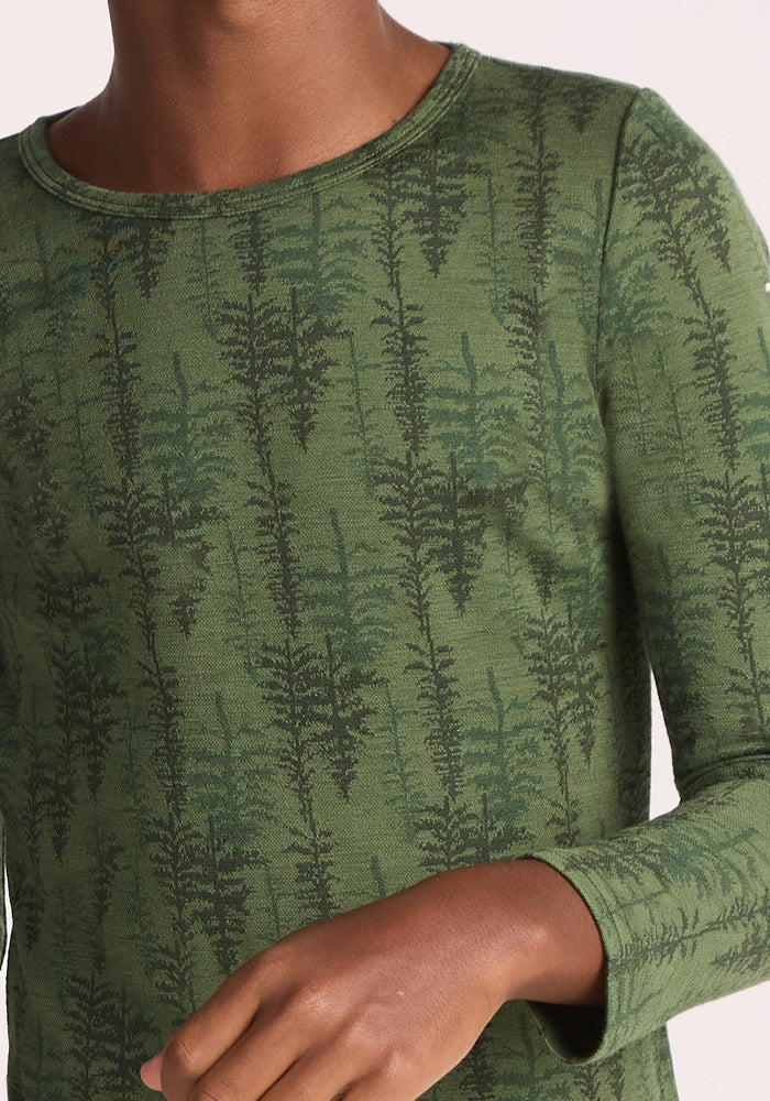 A child wearing the Woolx Kids Explorer Base Layer Top - Forest Friends, featuring long sleeves and a dark green fern pattern in moisture-wicking Australian Merino wool. Only the lower face, upper body, and one arm are visible.