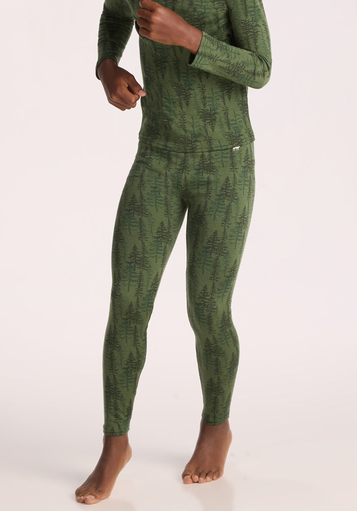 A barefoot person stands against a plain light background, wearing Woolx Kids Explorer Base Layer Bottoms - Forest Friends. Their top and head are not visible in the image.