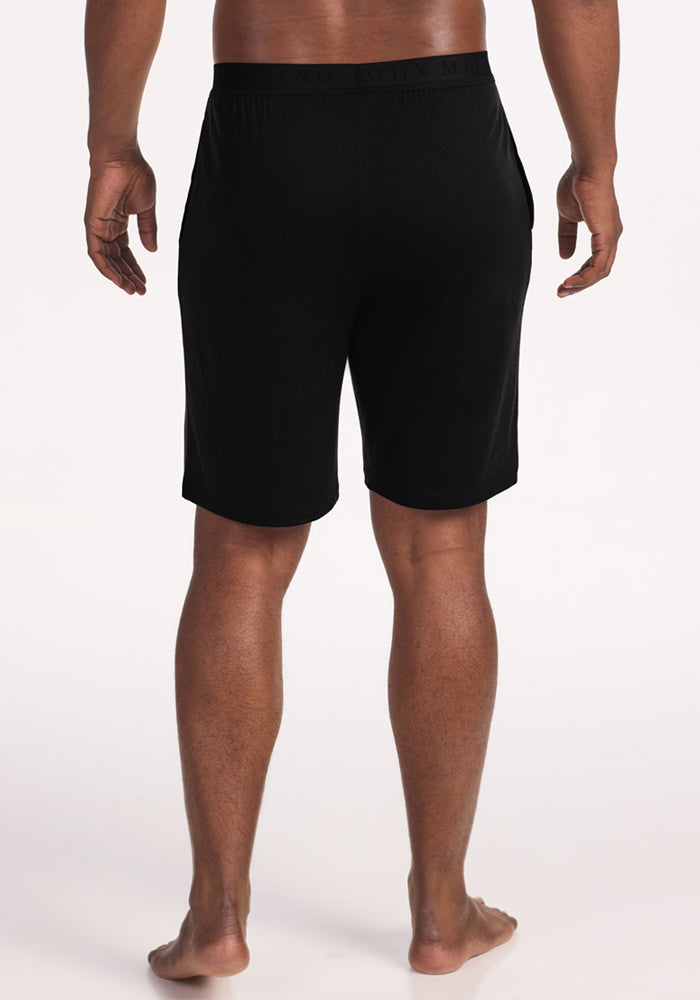 Man barefoot from behind, wearing Woolx Archer Lounge Shorts in black, against a plain light background.