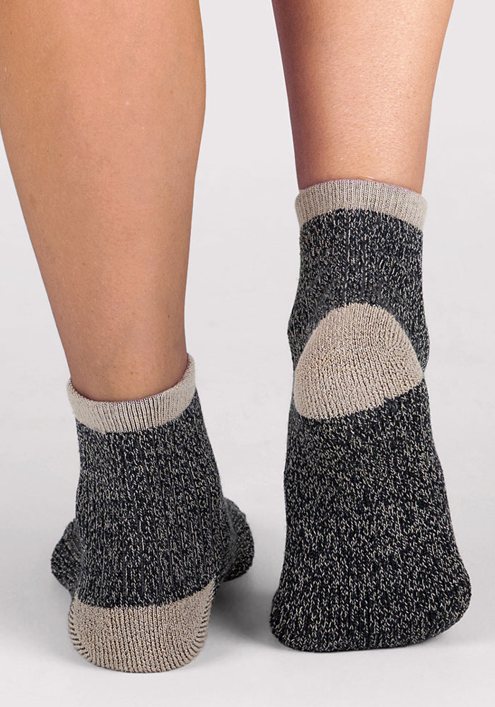 A close-up of two feet in Woolx Womens Cozy Mini Crew Socks - Black, featuring gray speckle, heel, and cuff accents, shown standing on a light surface.