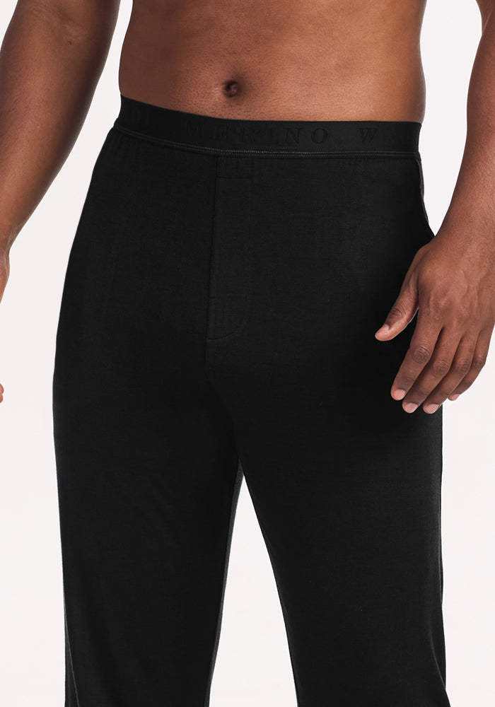 A person wears Woolx Arlo Lounge Pants - Black with a black elastic waistband, shown waist to mid-thigh against a plain light background. These cozy pants are ideal for relaxing at home.