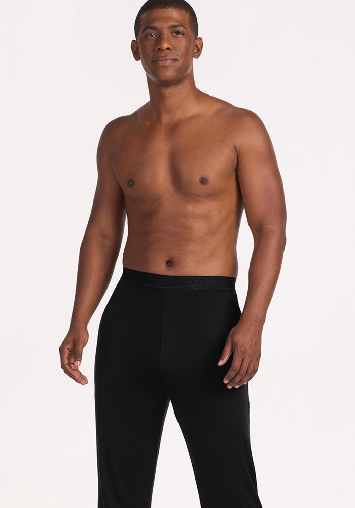 A man stands shirtless against a plain light background, facing forward with a neutral expression and arms by his sides, wearing Woolx Arlo Lounge Pants in Black.
