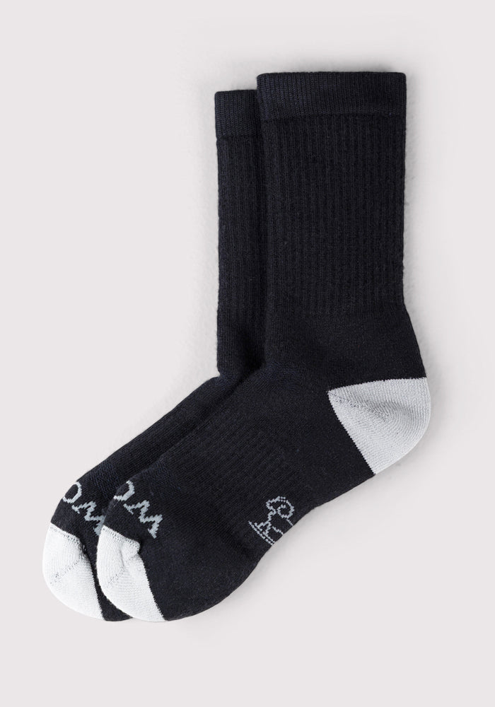 A pair of Woolx Mens Core Crew Socks in black with white heels, toes, and logos, plus writing on the toes, shown on a light grey background.