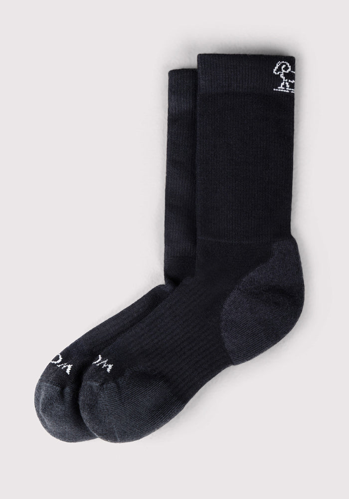 The Woolx Mens Harbor Crew Sock in black features dark gray heels and toes, a small white embroidered design near the top of one sock, and is displayed on a light gray background.