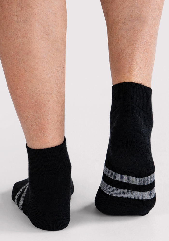 Two legs, seen from behind, wear Woolx Mens Rambler Ankle Sock - Black with two gray cuff stripes, resting on a light background to showcase the socks’ comfort, stylish design, and moisture-wicking features.
