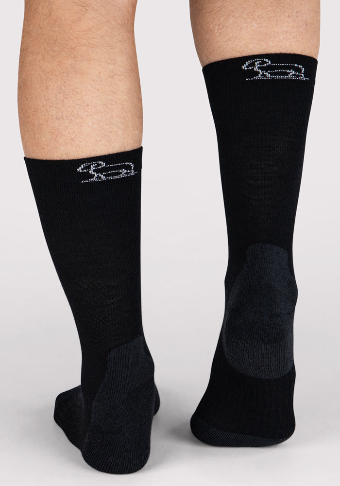 A close-up of two legs wearing Woolx Mens Harbor Crew Sock - Black, featuring a small white dachshund near the top and dark gray heel and toe patches. Made of Merino wool for comfort.