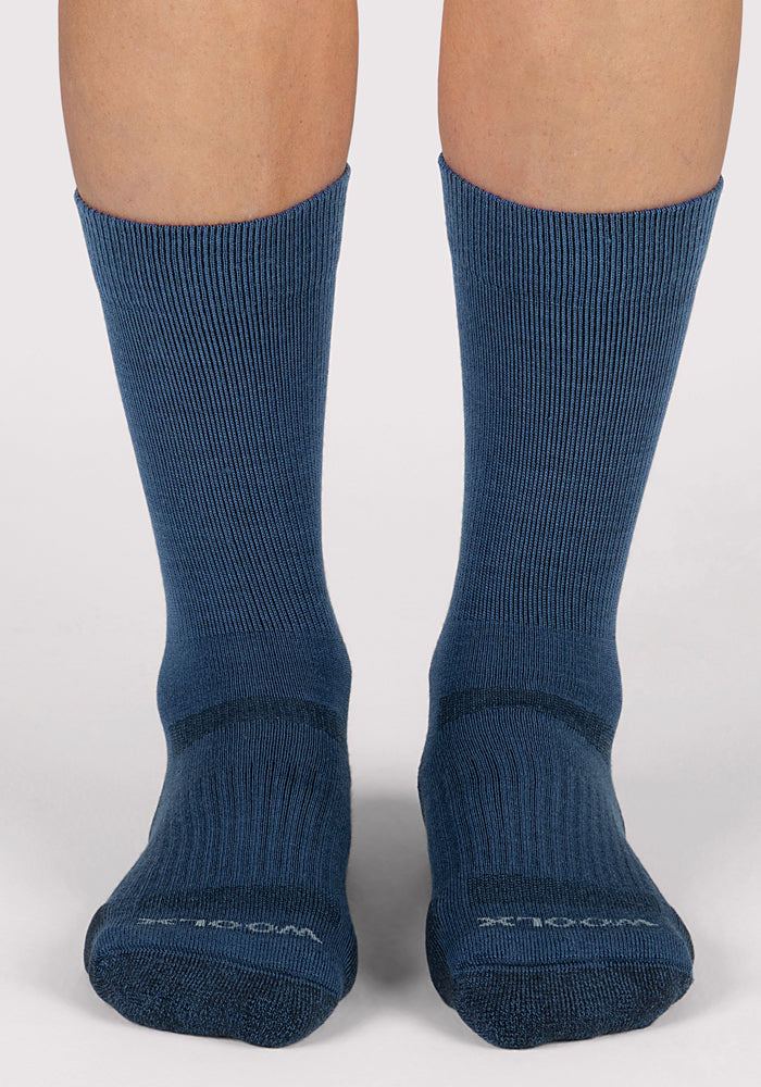 A pair of feet wears Woolx Womens Harbor Crew Socks in Majolica Blue, standing on a light surface. The ribbed, breathable socks reach mid-calf, featuring slightly darker toes and heels.