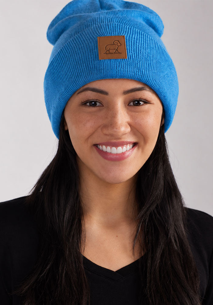 Woman smiles in a blue Baylor Beanie by Woolx, featuring a brown patch, paired with a black shirt on light background.