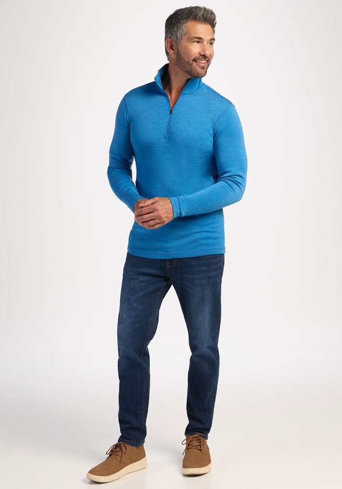 Smiling man wears Woolx Explorer 1/4 Zip - Blue Razz, jeans, and tan shoes against a plain white background.