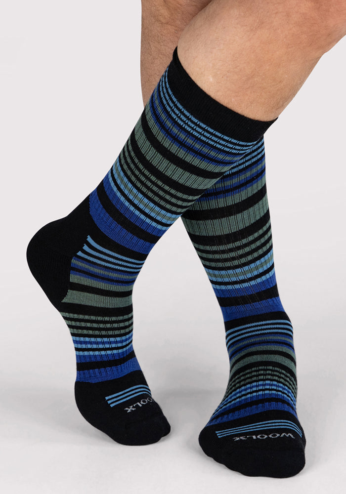 A person models Woolx Men's Everyday Crew Socks in Black Stripe, standing with one foot crossed over the other on a light gray background.