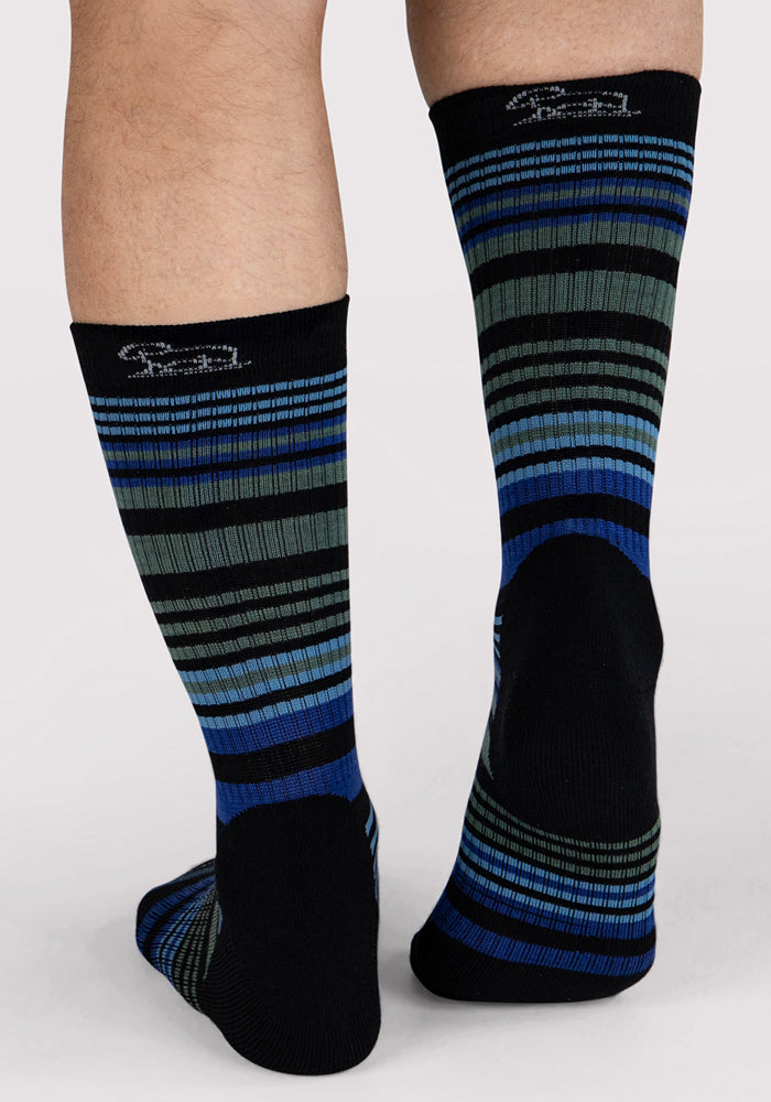 A pair of legs wear Woolx Mens Everyday Crew Socks - Black Stripe, featuring black Merino wool with blue, green, and gray stripes. The heels and toes are solid black. These naturally moisture-wicking socks ensure all-day comfort.