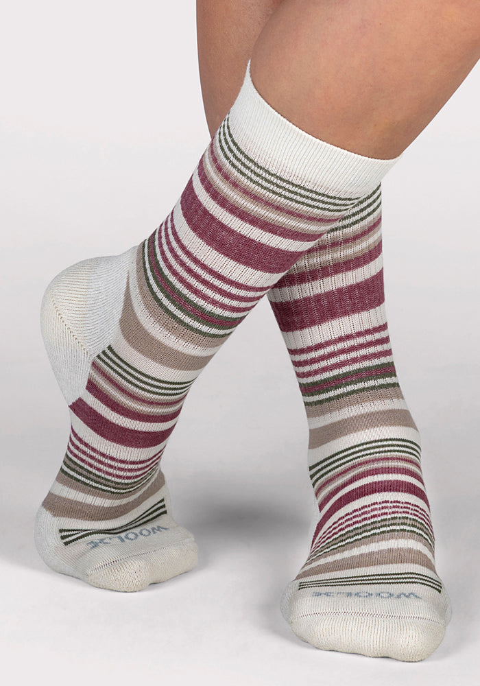 A pair of crossed feet wear Woolx Womens Everyday Crew Socks in Buttercream Stripe, featuring moisture-wicking, cushioned white fabric with horizontal stripes in burgundy, beige, olive green, and gray.