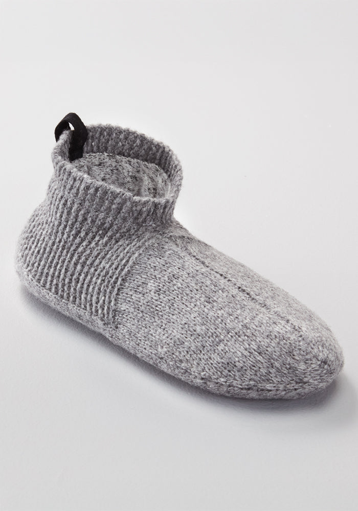 The Woolx Womens Gripper Slippers in Gentle Grey feature a single merino wool knit design, ribbed ankle cuff, and black pull tab at the back, shown on a plain light background.