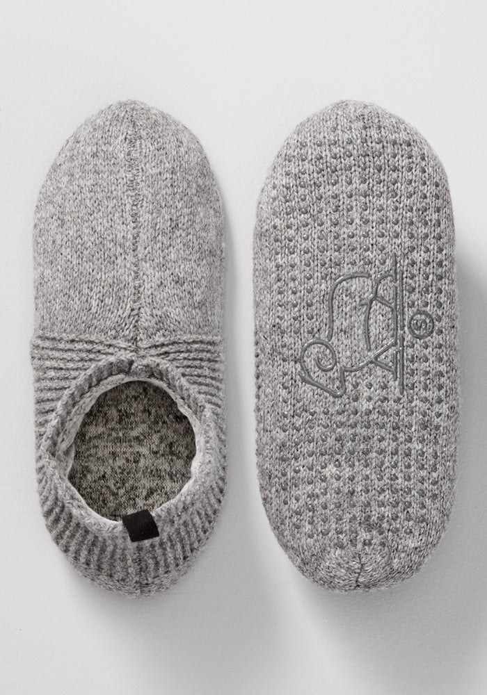 Woolx Mens Gripper Slippers in Gentle Grey feature a textured knit pattern; one slipper shows the top with an opening, while the other reveals a sole decorated with a stylized animal, possibly a penguin.