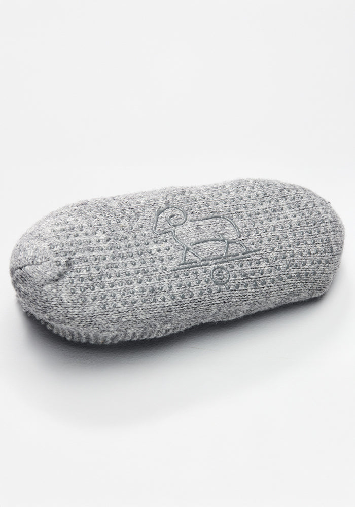 A single Woolx Mens Gripper Slippers - Gentle Grey lies flat on a white background, featuring an embroidered outline of a kiwi bird on its surface.