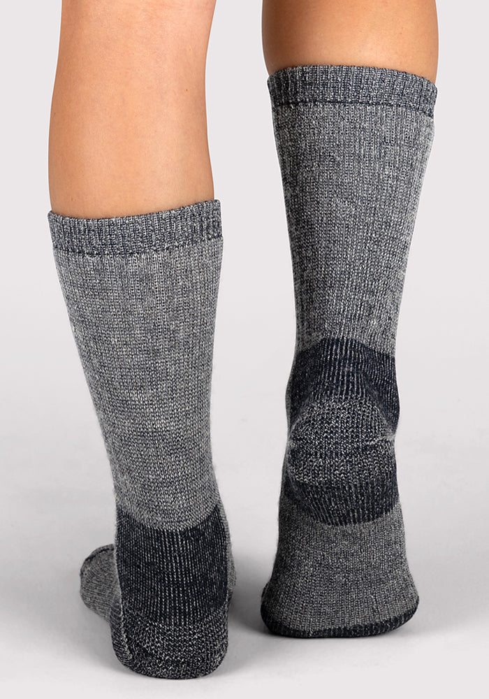 A person wearing Woolx Womens Extreme Crew Socks in Charcoal Heather stands on a light background. These heavyweight merino wool socks are perfect for keeping feet warm during cold weather.
