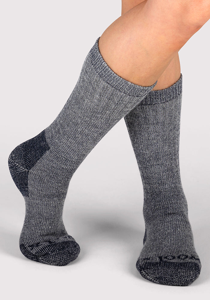 A person wearing Woolx Womens Extreme Crew Socks in Charcoal Heather with darker gray accents on the toes and heels, standing on a light gray background.
