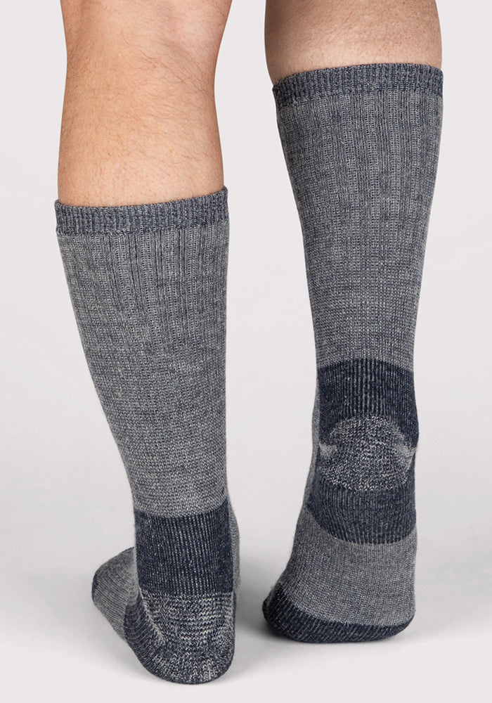 A close-up of a person's lower legs and feet wearing Woolx Mens Extreme Crew Socks in Charcoal Heather, standing on a light background.