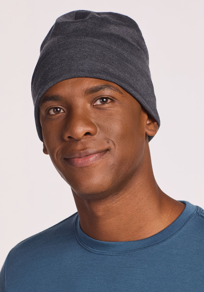 A man in a Woolx Journey Hat - Cinder Melange and a blue shirt smiles gently at the camera, set against a simple light background.