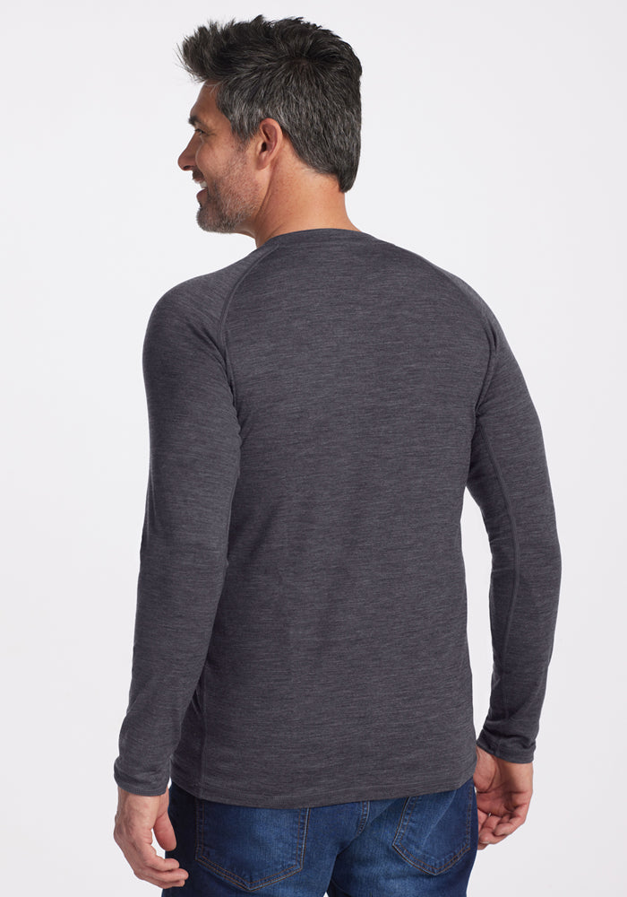 A man with short dark hair and a beard stands facing away from the camera, wearing the Woolx Essential Tee in Cinder Melange and blue jeans, set against a plain white background.