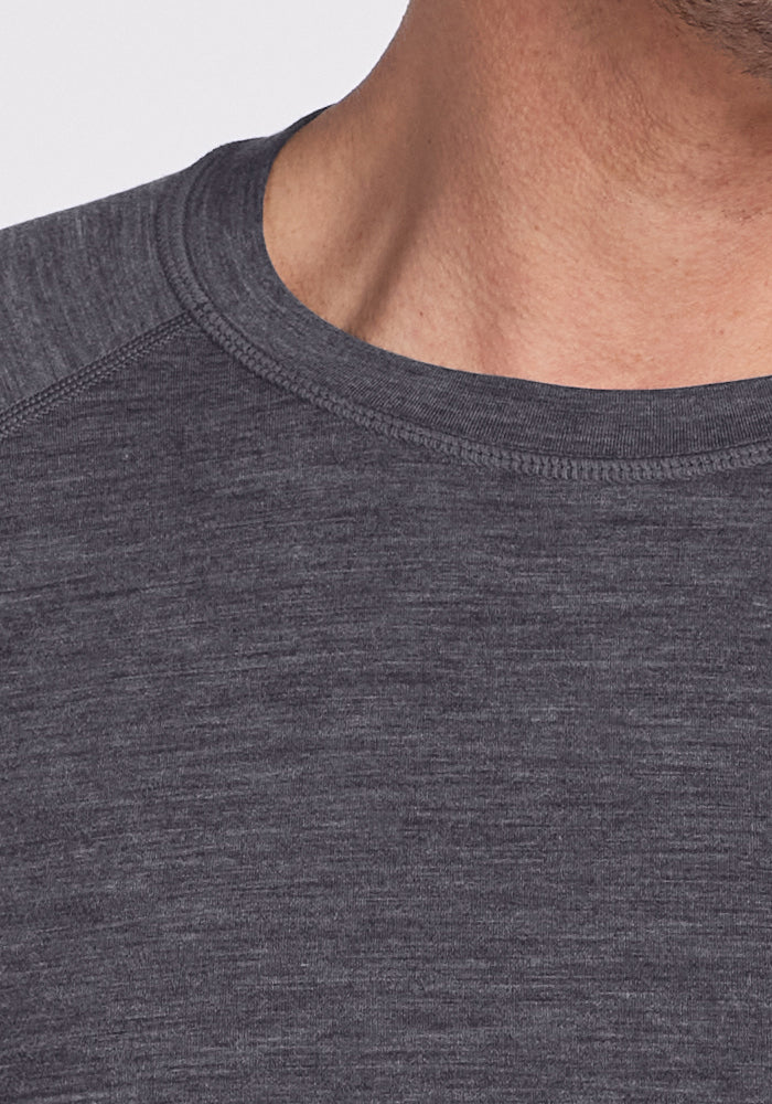Close-up of a person's neck, lower face, and upper chest wearing the Woolx Essential Tee in Cinder Melange, a temperature regulating heathered dark gray crew neck. Beard stubble and part of their shoulder are also visible.