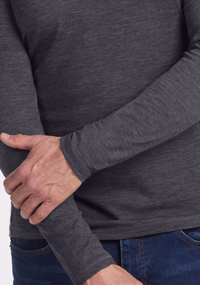 A person wearing the Woolx Essential Tee in Cinder Melange and blue jeans holds their left forearm with their right hand against a plain white background.