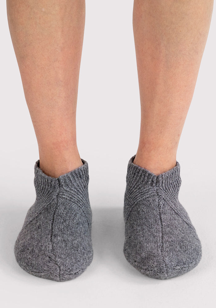 A pair of feet wear Woolx Womens Gripper Slippers in Gentle Grey, shown from the front against a plain white background.
