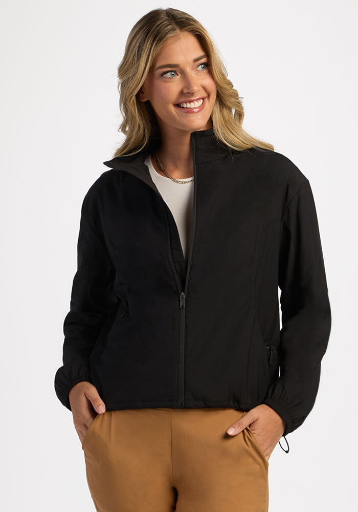 Woman smiling, wearing the Woolx Cooper Windbreaker - Black over a white shirt and tan pants.